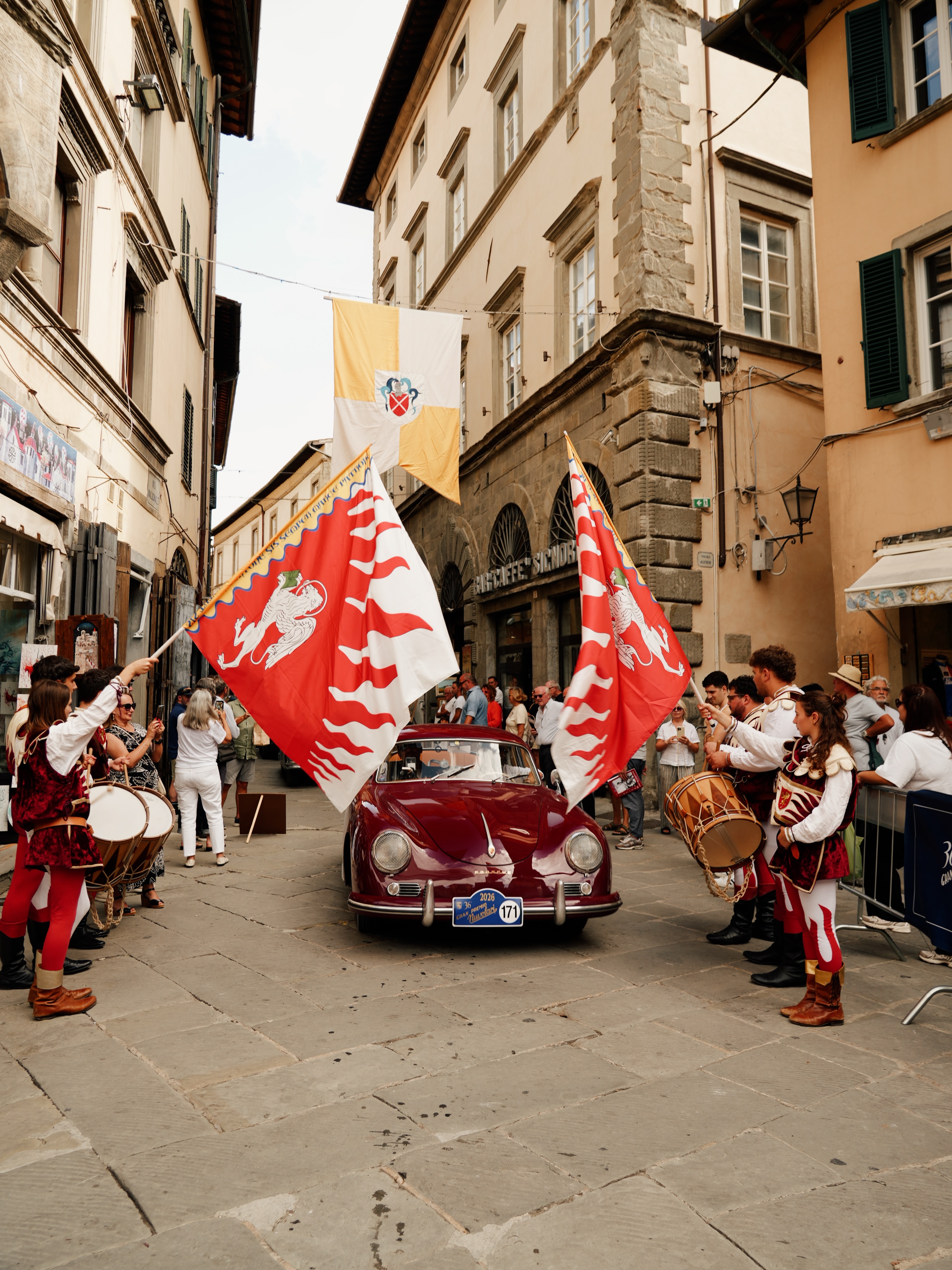 Princess Grace driving between flags and spectators in a historic centre