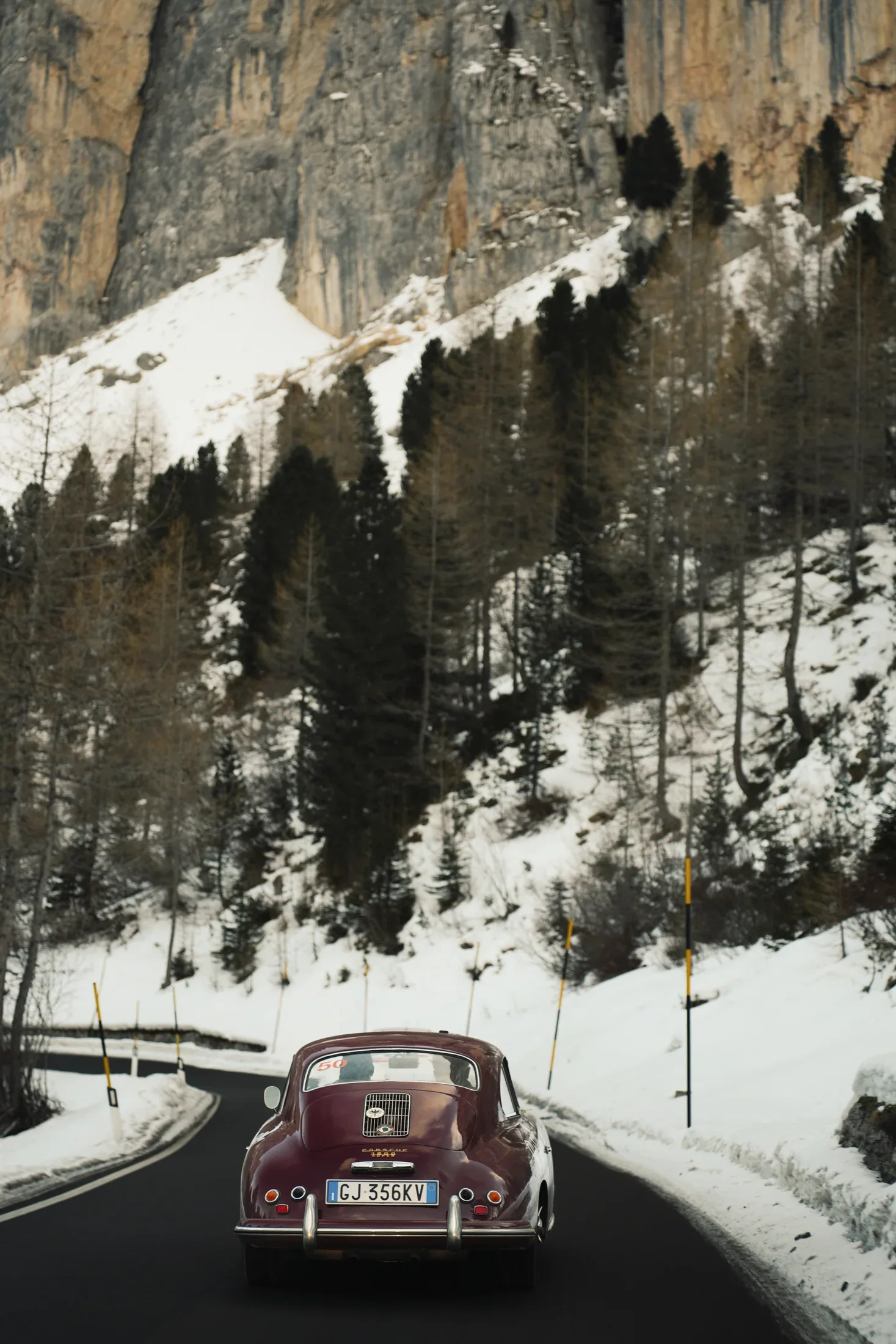 The Porsche 356 driving on a snow-lined mountain road.