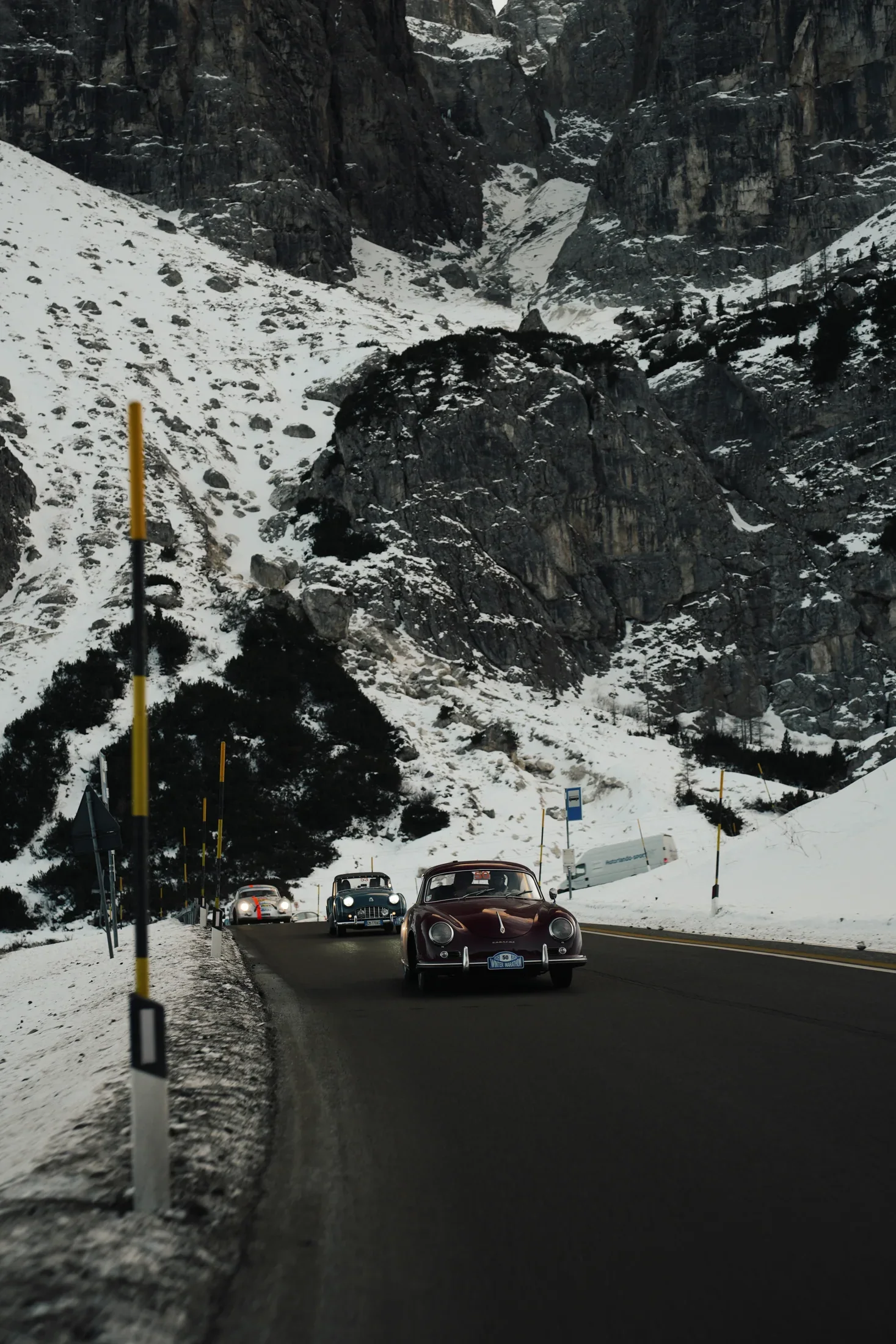 The Porsche 356 on a dramatic alpine road under rock walls.