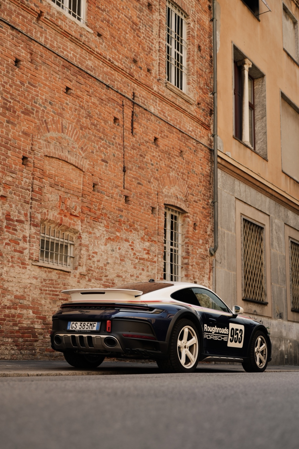 Abeba, the Porsche 992 Dakar in Roughroads livery, beside a red brick wall in Milan