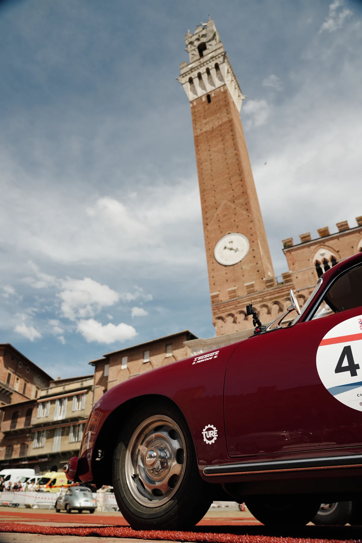 A red classic racing car in Piazza del Campo with the Torre del Mangia during the Mille Miglia
